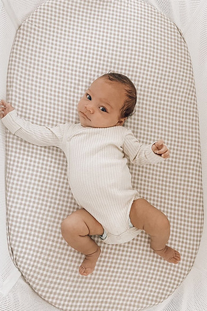 baby laying awake on beige gingham fitted sheet in bassinet