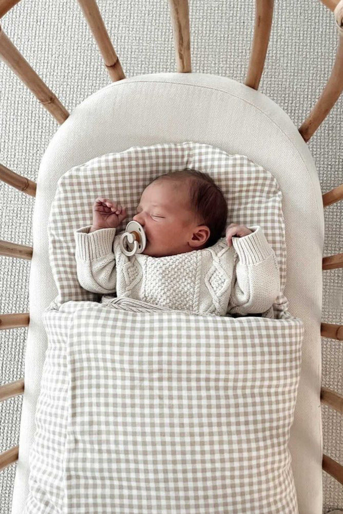 baby sleeping in beige gingham wool wrap in bassinet
