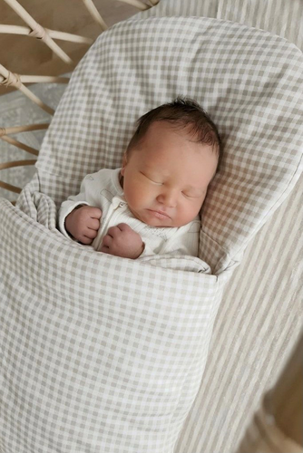 baby sleeping in beige gingham wool wrap in bassinet