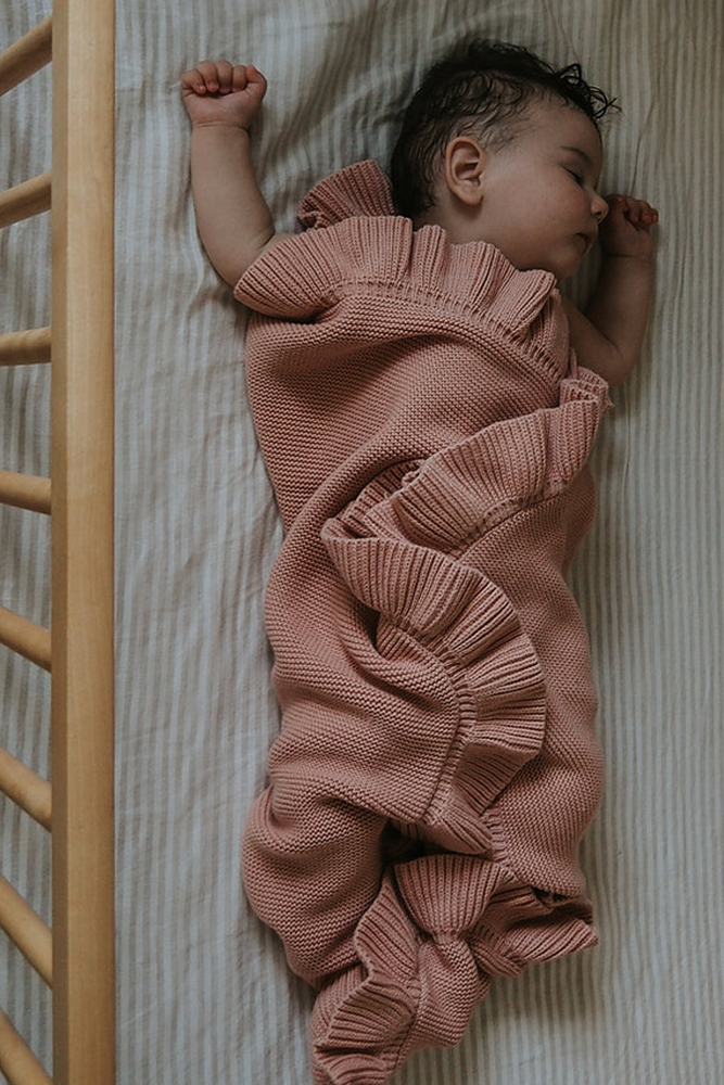 Baby wrapped in dusty pink frill knitted blanket sleeping in cot