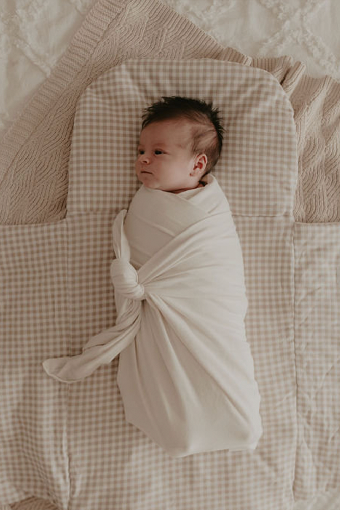 Baby swaddled and laying on top of gingham Bundl wool wrap 