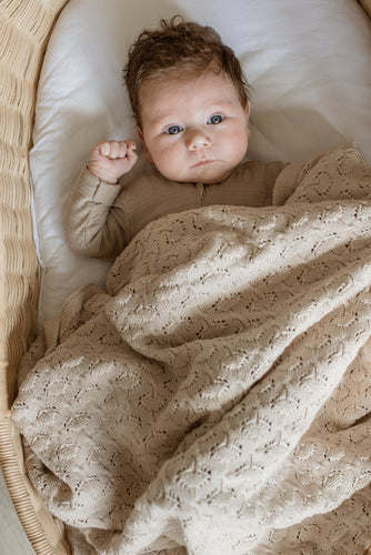 baby with beige organic blanket in bassinet