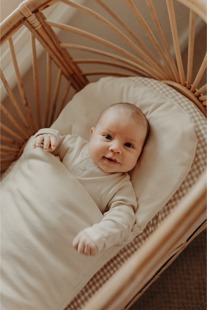 smiling baby in wool wrap in rattan cane bassinet