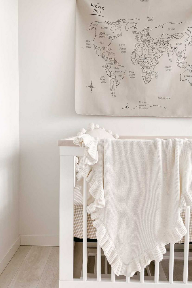 whit knit baby blanket on cot with world map on wall