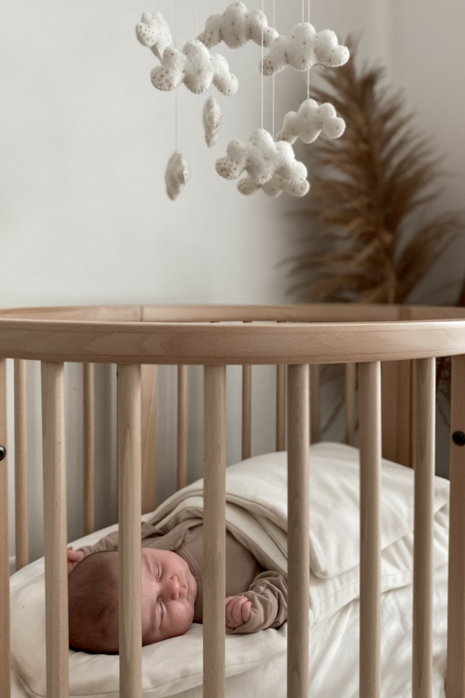 Baby sleeping in natural wood cot in wool wrap with cloud mobile